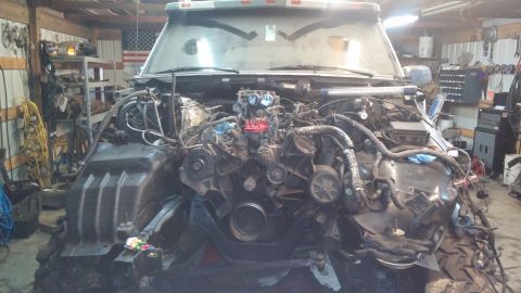 1995 Ford Bronco - The engine bay of a vehicle is disassembled, showing the engine and surrounding components in a workshop setting.