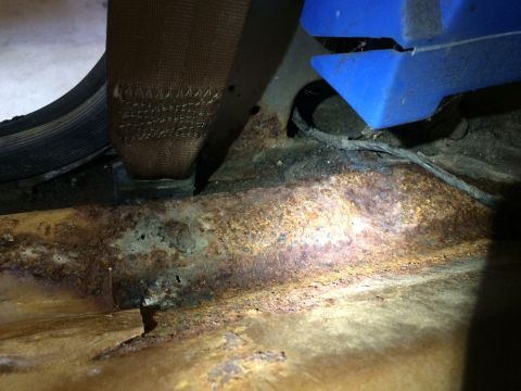1991 Ford Bronco - The floor pan of a vehicle shows significant rust and damage, with a seatbelt visible.