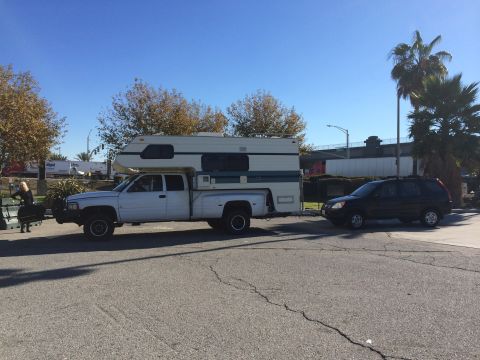1986 Yugo GV - A white pickup truck with a camper is parked next to a black SUV on a sunny day.