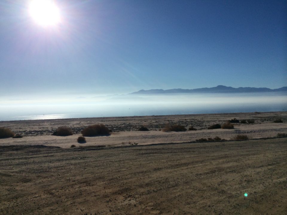 Desert landscape with sun glare, haze over water, and distant mountains