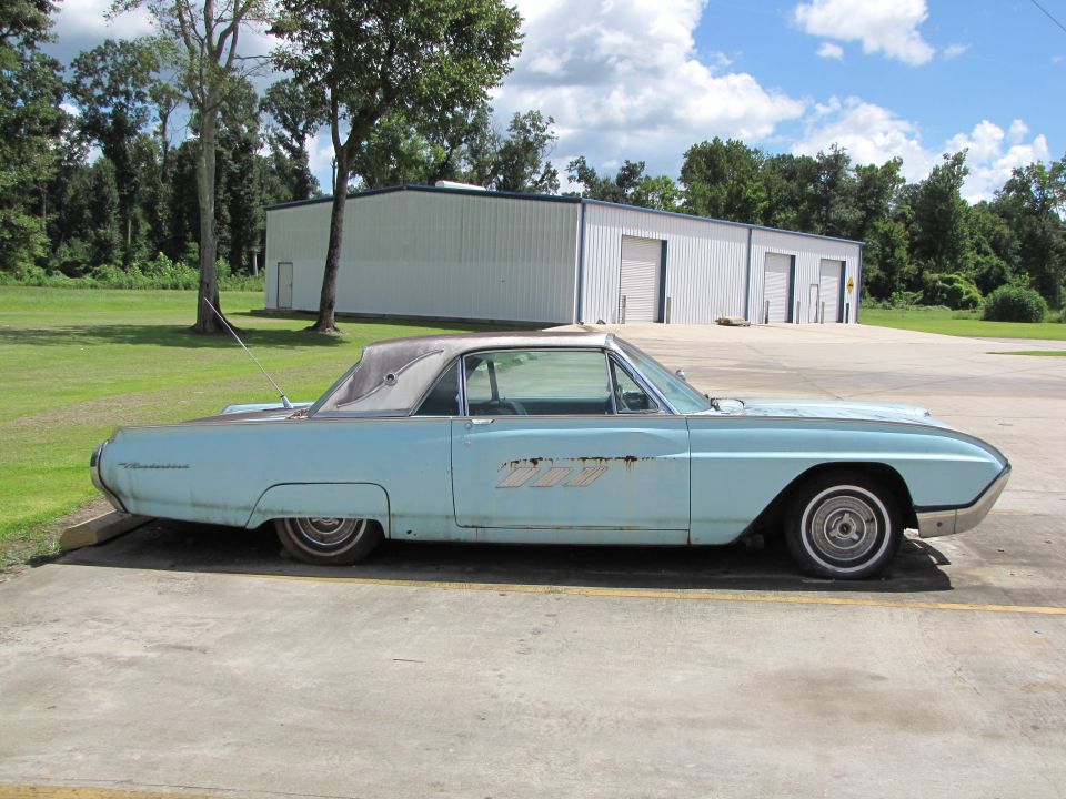Light blue 1963 Ford Thunderbird coupe, side view. White roof, rusty side emblem