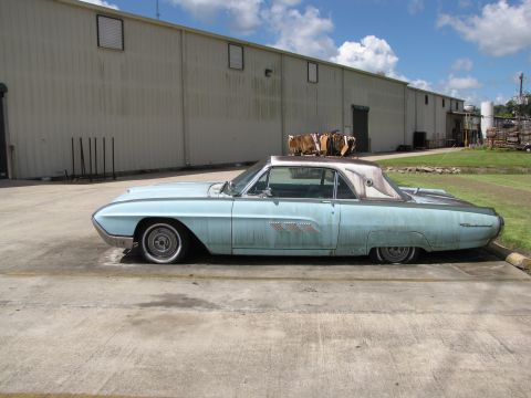 1963 Ford Thunderbird - A light blue 1963 Ford Thunderbird coupe with a white convertible top is parked outside a warehouse.