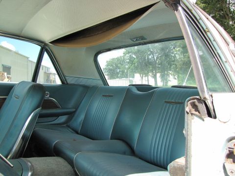 1963 Ford Thunderbird - The interior of a vintage automobile, blue vinyl seats and a white perforated headliner, is shown from the rear.