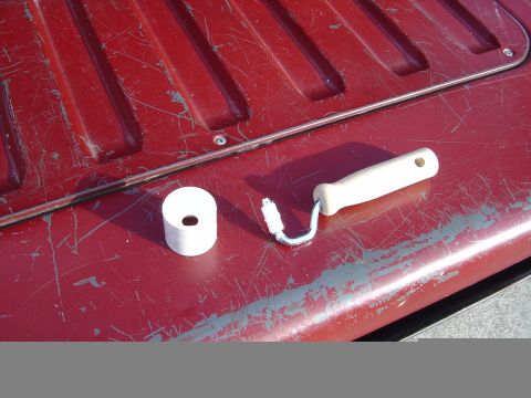 1986 Ford Bronco - A paint roller and a roll of tape sit on a weathered red surface, possibly a vehicle's tailgate, suggesting a restoration project.