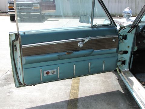 1963 Ford Thunderbird - The interior door panel shows wood grain trim, a chrome handle, and two buttons, with another vehicle visible through the window.