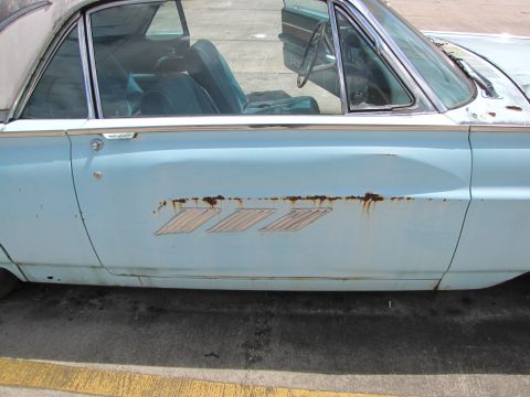 1963 Ford Thunderbird - A light blue 1963 Ford Thunderbird shows significant rust damage on its side trim.