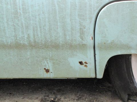 1963 Ford Thunderbird - Close-up of a weathered car's side panel reveals significant rust damage and a visible tire.