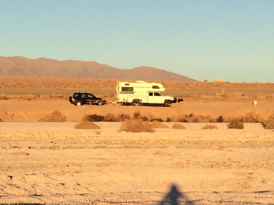 Black SUV towing a white camper on a desert road