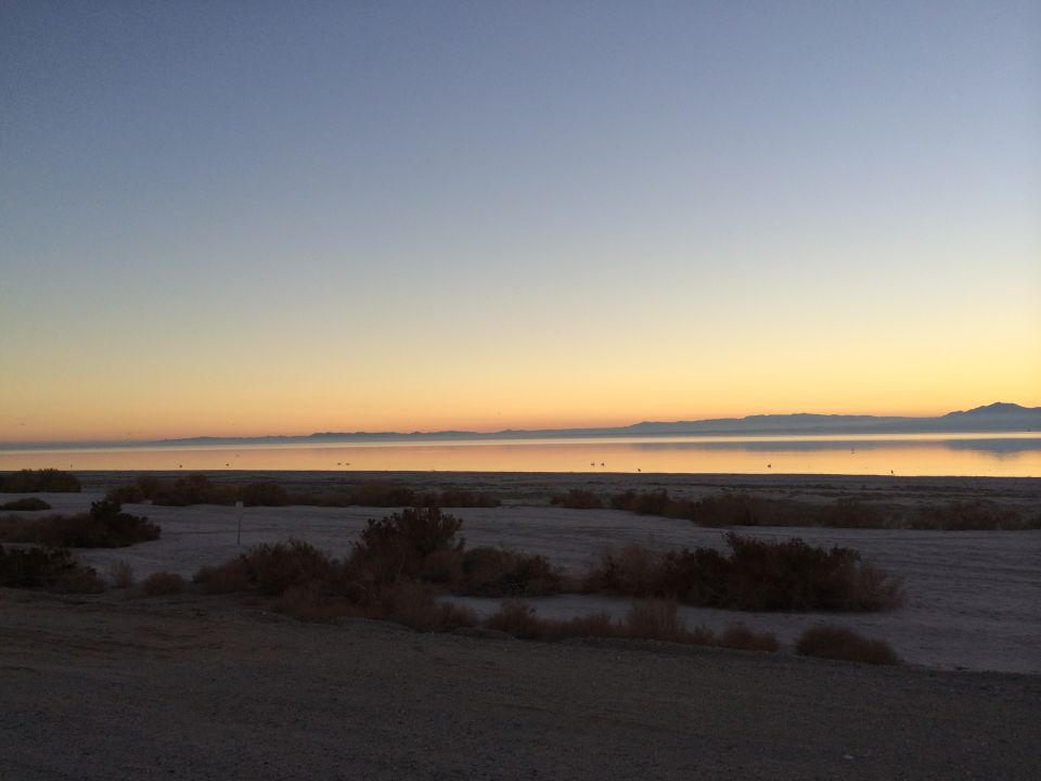 Desert scrub and dry lakebed with mountains on the horizon at sunset