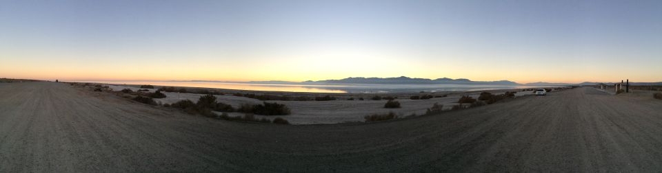 Dirt road leading to a body of water with mountains in the distance at sunrise