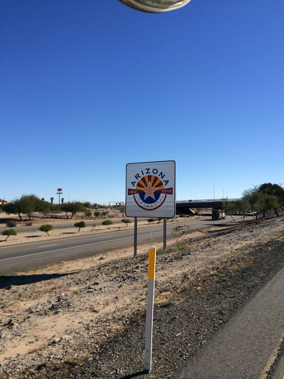 Arizona Centennial sign on roadside with blue sky and desert landscape