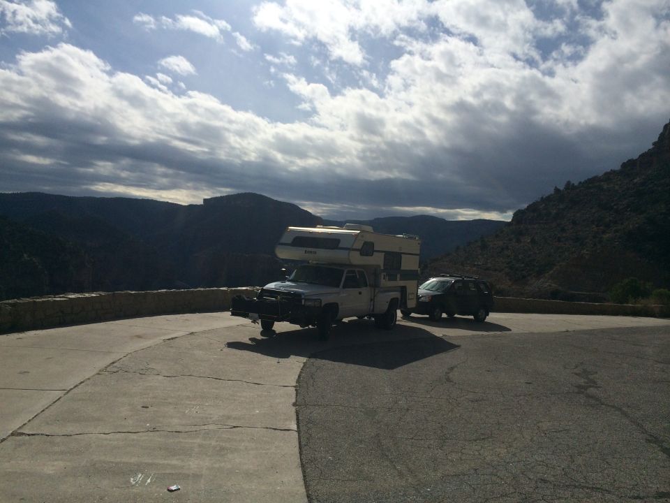 Pickup truck with camper shell and an SUV parked on a scenic overlook with mountains in the background