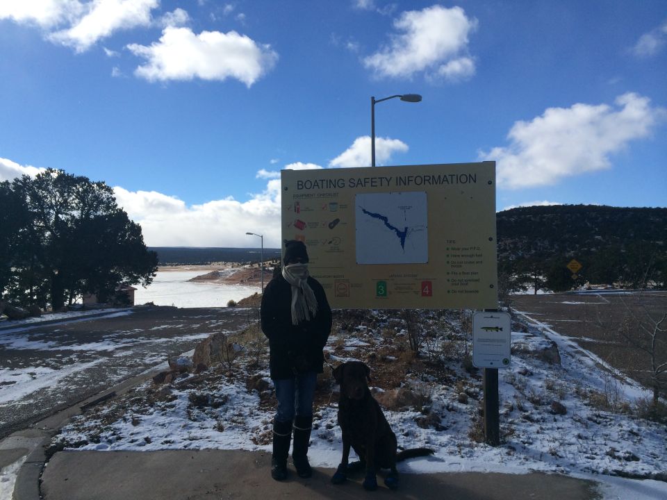 Person and dog stand by a boating safety information sign near a frozen lake