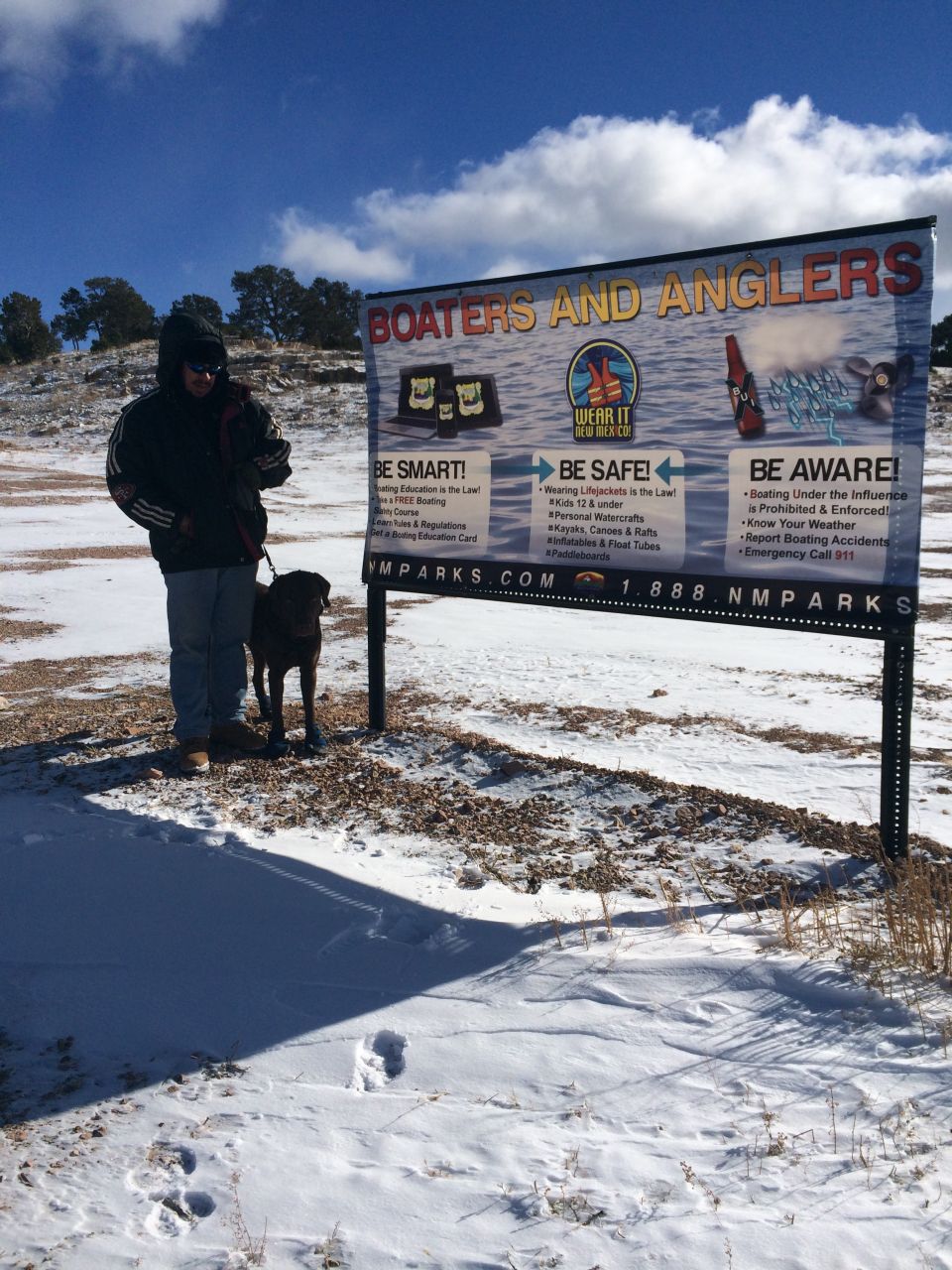 Person with dog standing next to a large sign about boaters and anglers