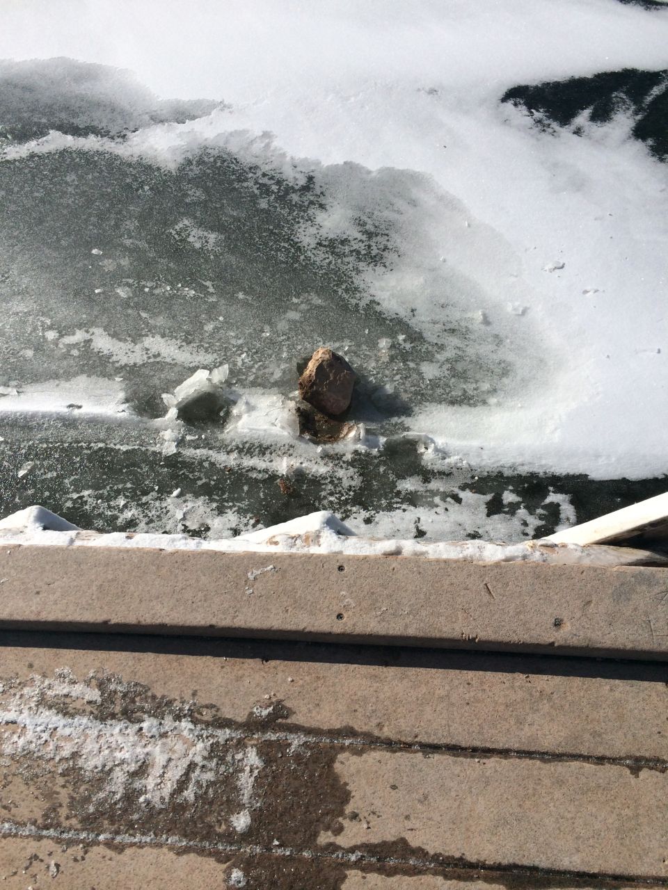 Rock in partially frozen water with snow and wooden planks