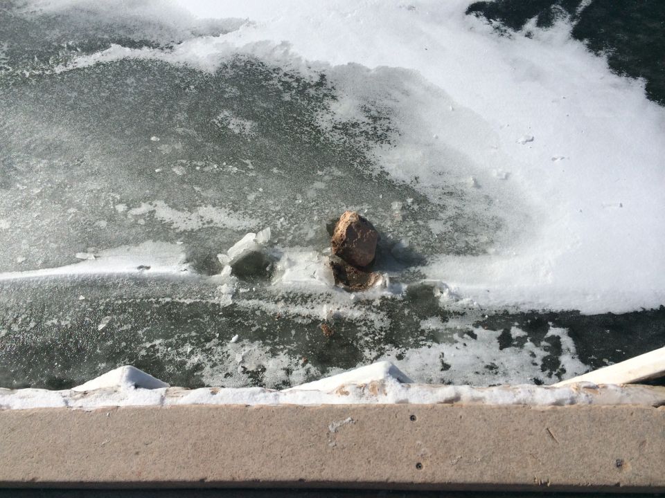 Rock partially submerged in icy water with snow on the bank