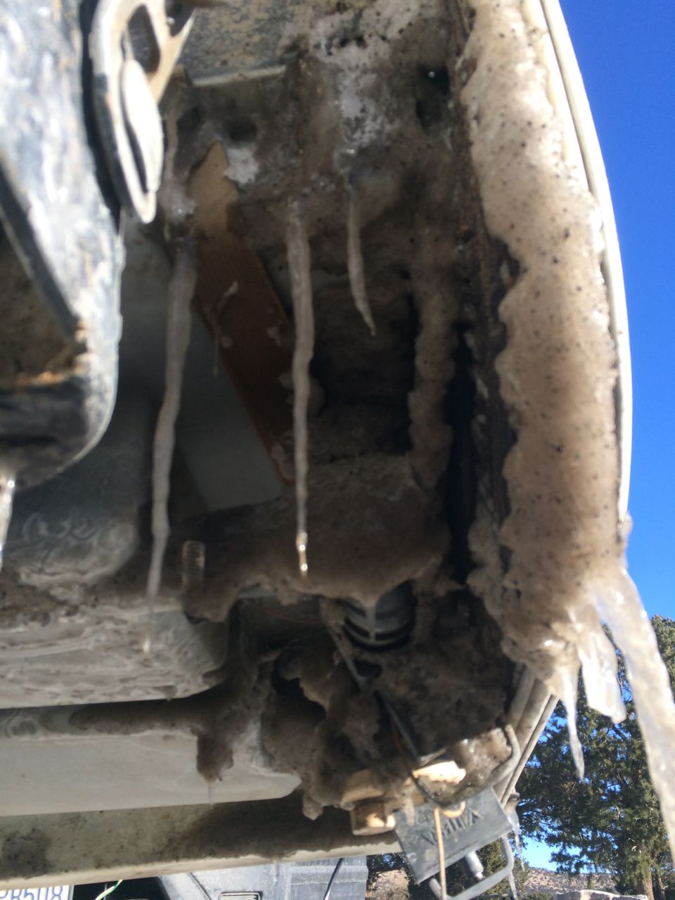 Frozen ice and snow buildup on the undercarriage of a vehicle, with icicles hanging down