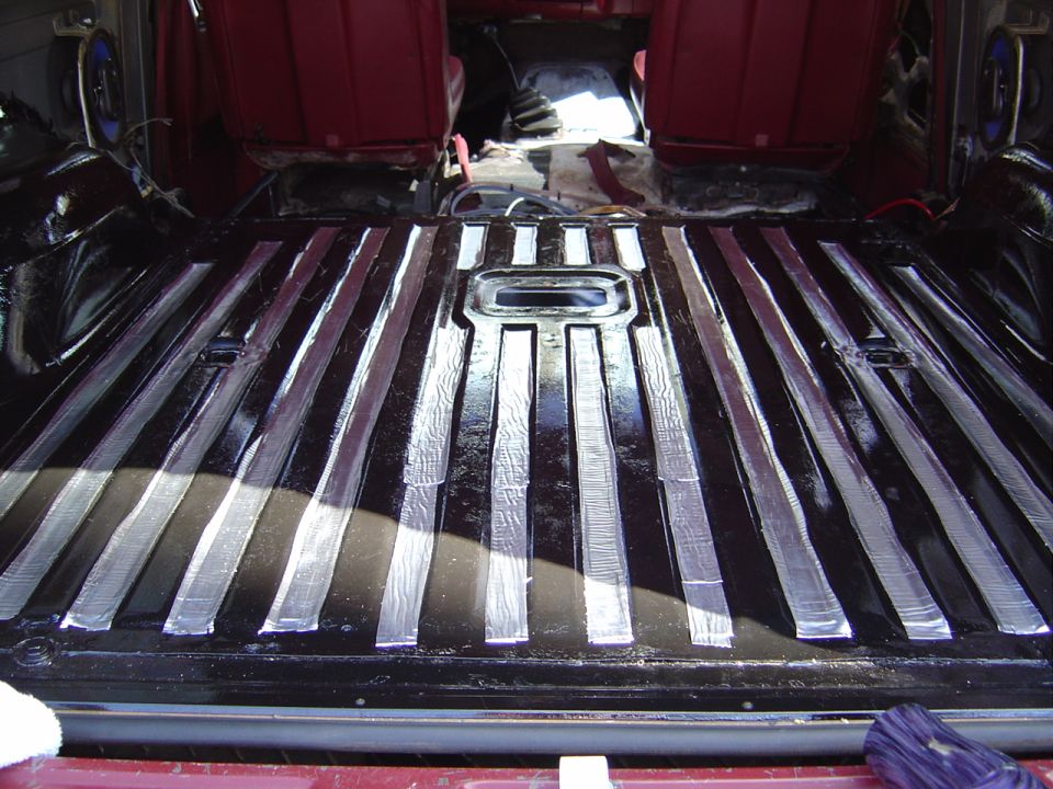 Rear cargo floor of SUV with black ribbed metal, sanded stripes, and red interior panels