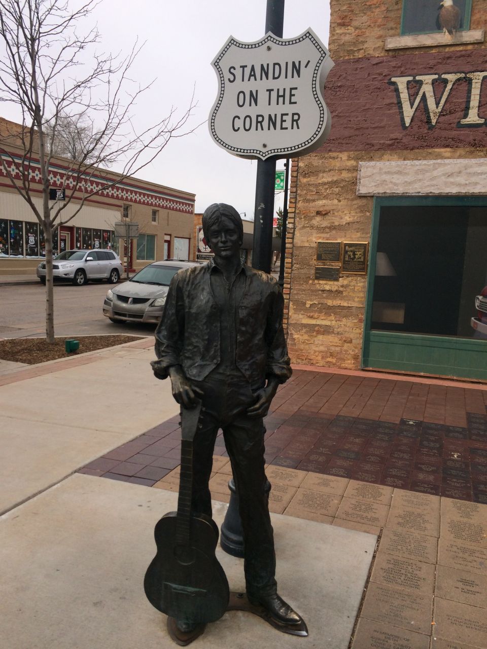 Statue of a man holding a guitar, standing on a street corner with a sign that says 'Standin' on the Corner'