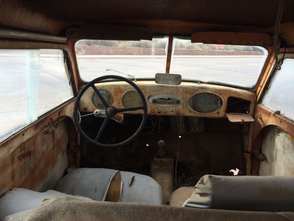 Interior of a rusty car with a black steering wheel and two gauges