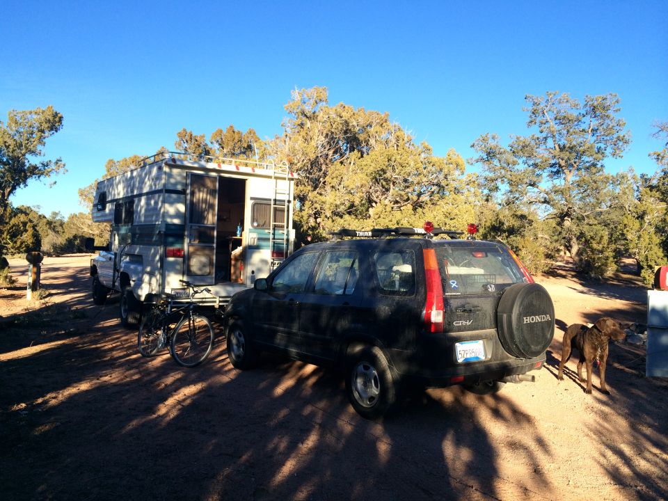 Black Honda CR-V with spare tire, rear view, parked next to a camper on a truck
