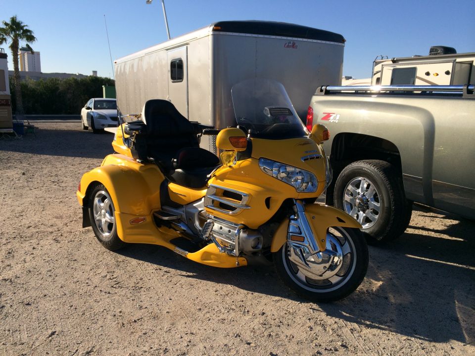 Yellow trike motorcycle parked next to a pickup truck and trailer