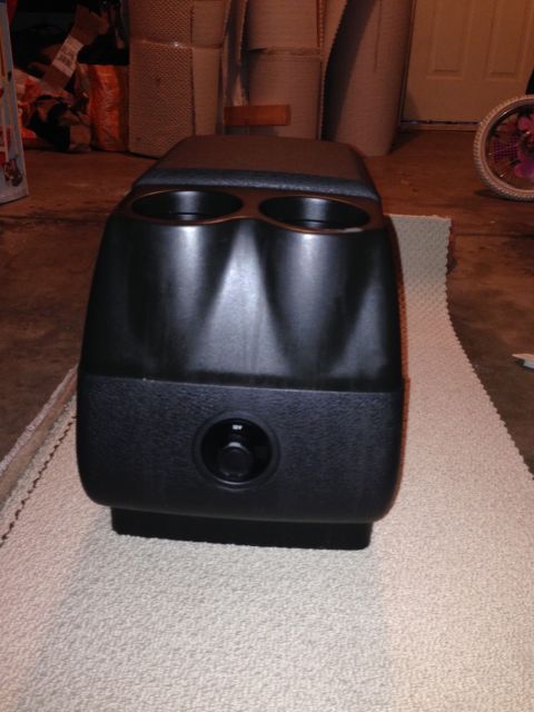 1995 Ford Bronco - A black vehicle center console with cup holders and a control dial sits on a rug in a garage.
