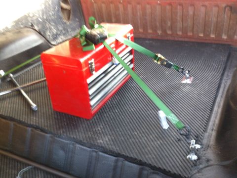 1986 Ford Bronco - A red toolbox is strapped down in the bed of a truck next to a spare tire.