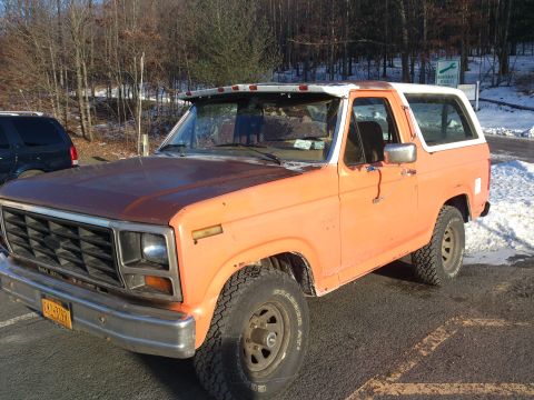 1986 Ford Bronco - This 1986 Ford Bronco is seen from a 3/4 front angle, parked in a lot with trees and snow.