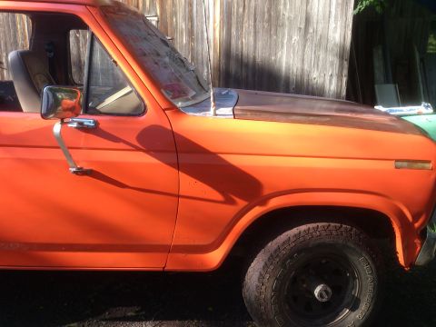 1986 Ford Bronco - Side profile of an orange SUV, highlighting its door and fender. The vehicle's styling suggests it is from the early 1980s.