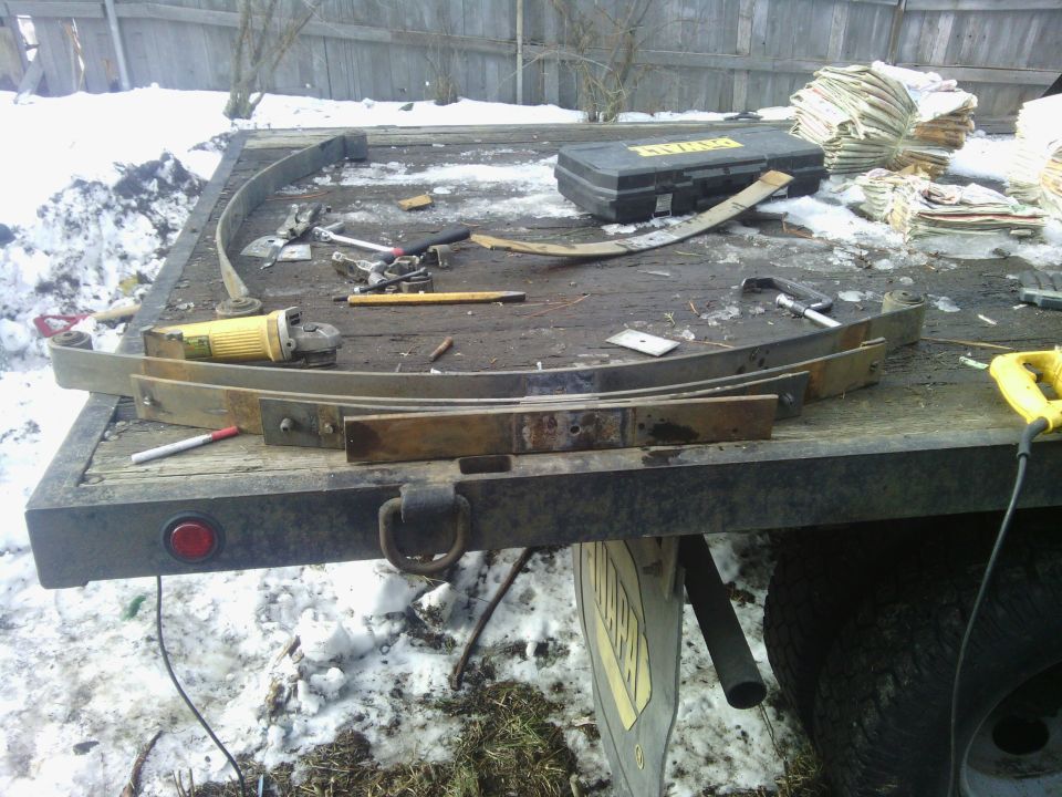 Leaf springs, angle grinder, and a DeWalt toolbox on a trailer bed with snow on the ground