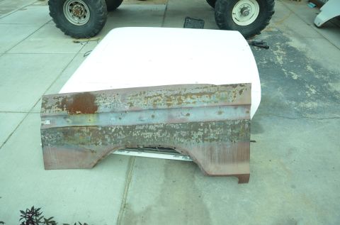 1979 Ford Bronco - A heavily rusted quarter panel rests on a white hood, with large off-road tires visible behind.