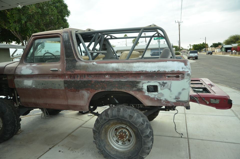 Side view of a 1978 Ford Bronco with a roll cage installed, body in primer and red paint, tailgate removed
