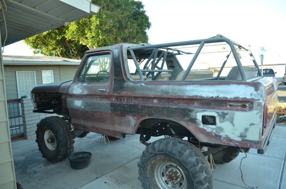 Rusty 1978 Ford Bronco with roll cage, lifted on large tires, undergoing body work