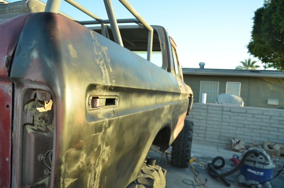 Red and black Ford Bronco body with roll cage, missing taillight, and large tires