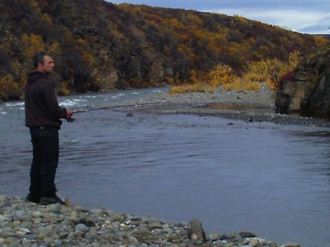 1990 Ford F-250 - Man fishes from the bank of a river with trees showing fall colors on the opposite bank.
