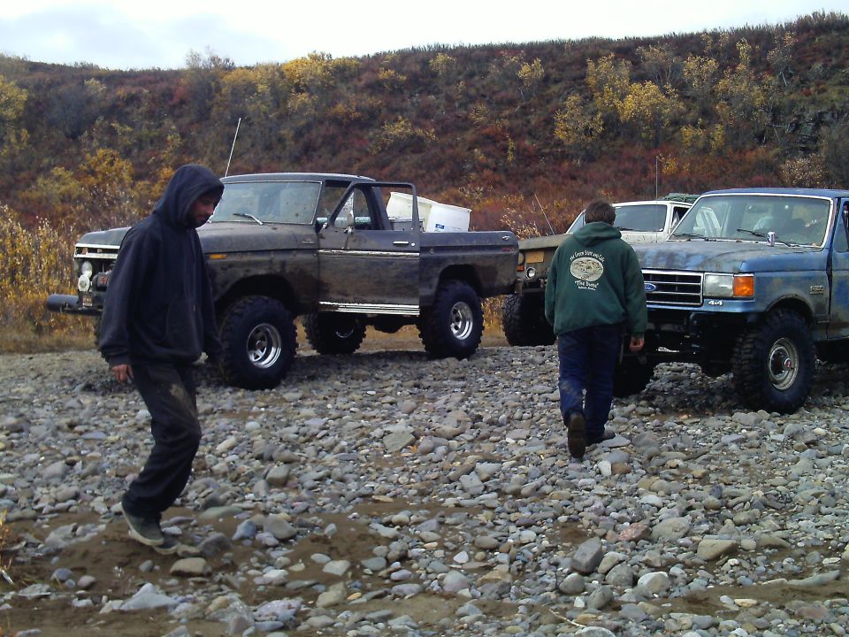 Two pickup trucks, one brown and one blue, parked on a rocky terrain. People are walking around them
