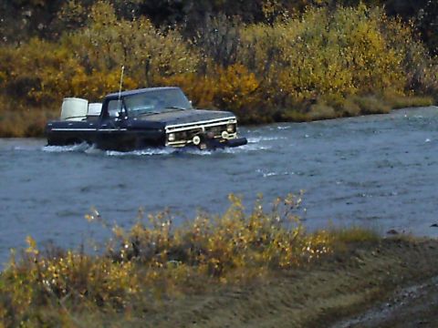 1990 Ford F-250 - A dark blue 1979 Ford F-Series pickup truck navigates through a shallow river surrounded by autumn foliage.