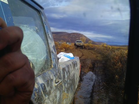 1990 Ford F-250 - Two trucks navigate a challenging muddy trail in a scenic, hilly landscape under a cloudy sky.