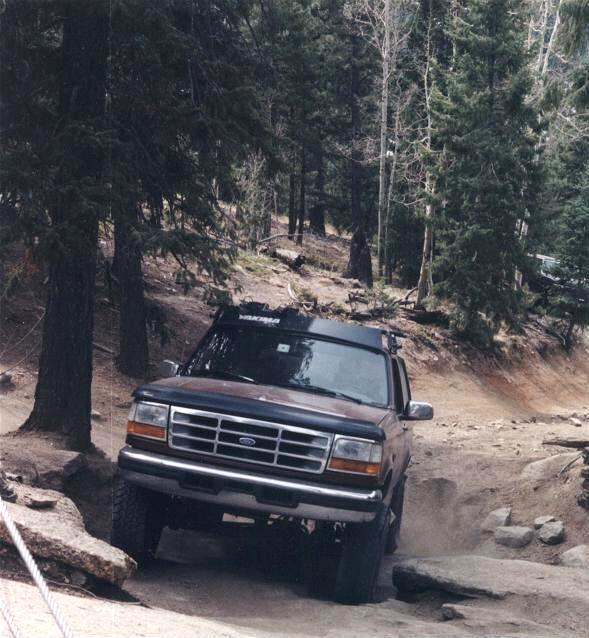 Brown Ford Bronco driving on a dirt road with trees