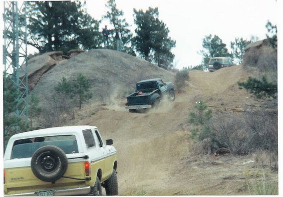 Yellow and white Ford Bronco and a dark green Ford pickup truck driving on a dirt hill