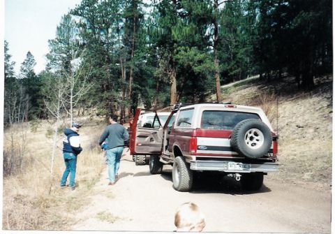 1996 Ford Bronco - Two-tone maroon and white SUV parked on a dirt road with trees in the background.