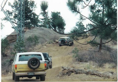 1996 Ford Bronco - Two SUVs navigate a steep dirt trail in a wooded, hilly area.
