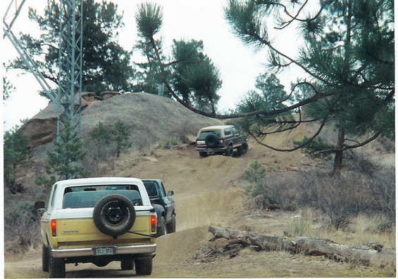 1996 Ford Bronco and another SUV driving on a dirt hill, spare tire on the back of the Bronco