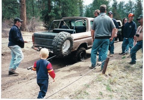1996 Ford Bronco - A group of people watch as a brown Ford Bronco gets stuck in the mud.