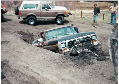 1996 Ford Bronco - A Ford truck is deeply mired in a muddy trench, while another vehicle watches from higher ground.