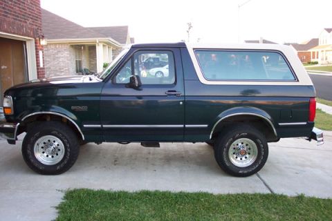 1992 Ford Bronco - A dark green 1992 Ford Bronco with a white top is parked in front of a brick garage.