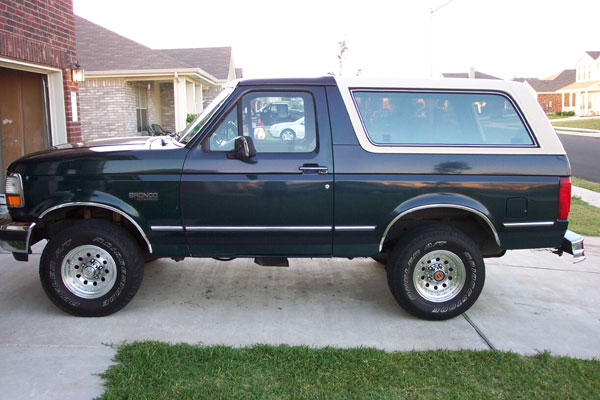 Dark green Bronco with white hardtop, driver-side profile on a suburban driveway
