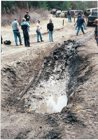 1996 Ford Bronco - A group of people observe a deep, muddy trench with standing water and tire marks.