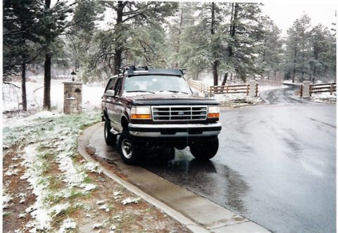 1996 Ford Bronco - Maroon 1996 Ford Bronco sits on a wet road with snow on the ground and trees in the background.